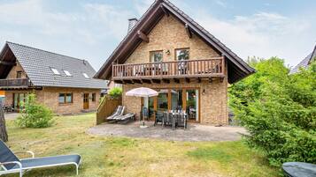 A two-story chalet with a balcony, outdoor seating, and a patio area.
