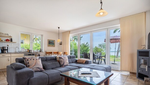 Ein modernes Wohnzimmer mit einem Ecksofa, einem Glastisch und Blick ins Freie durch große Schiebetüren.