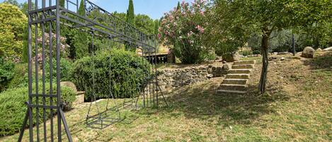 Una escalera de piedra conduce a una terraza de madera, rodeada de exuberante vegetación y plantas en flor.