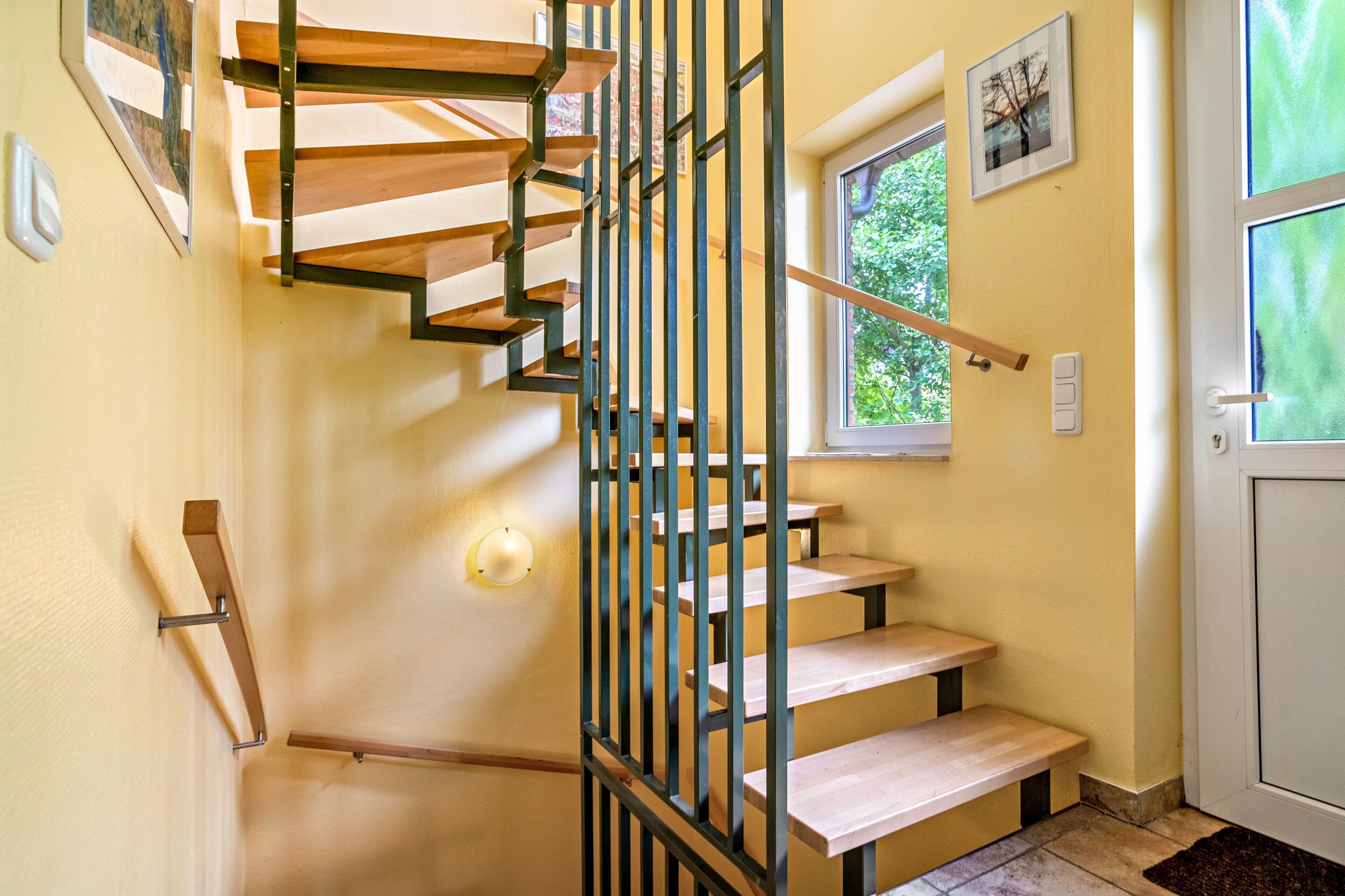 Eine Treppe mit hölzernen Stufen und Metallgeländern, eine Tür mit Fenster sowie eine Wandleuchte.