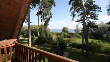 A wooden deck with a view of a grassy landscape and trees.