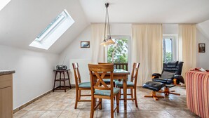 Ein Essbereich mit Tisch und Stühlen, einer Deckenleuchte und Blick durch das Fenster.