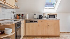 Eine moderne Küche mit Einbauofen, Mikrowelle und Kaffeemaschine, ausgestattet mit Holzschränken und einer gefliesten Spritzschutzwand.