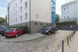 Ein Parkplatz mit Autos, ein Gebäude mit der Aufschrift '139 BLOC III' und eine Treppe, die zu einer oberen Ebene führt.