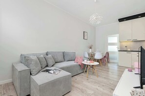 Un espace de vie moderne comprenant un canapé gris, une petite table à manger et un coin cuisine.