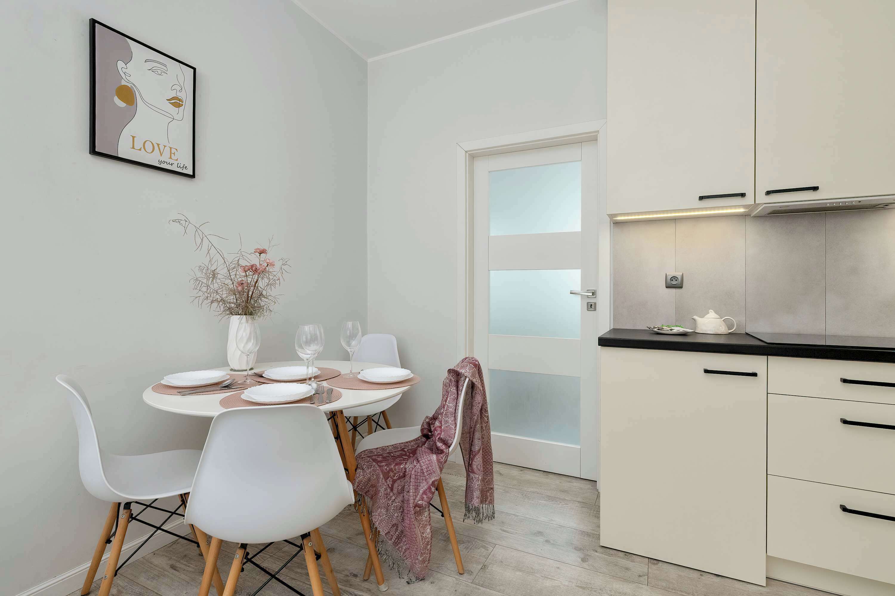 A modern kitchen with white cabinets, a black countertop, and a dining area with a white table set for four.