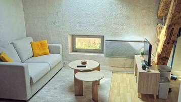 A modern living room with a sloped ceiling, a sofa with yellow cushions, a coffee table, a television, and a small side table with a plant.