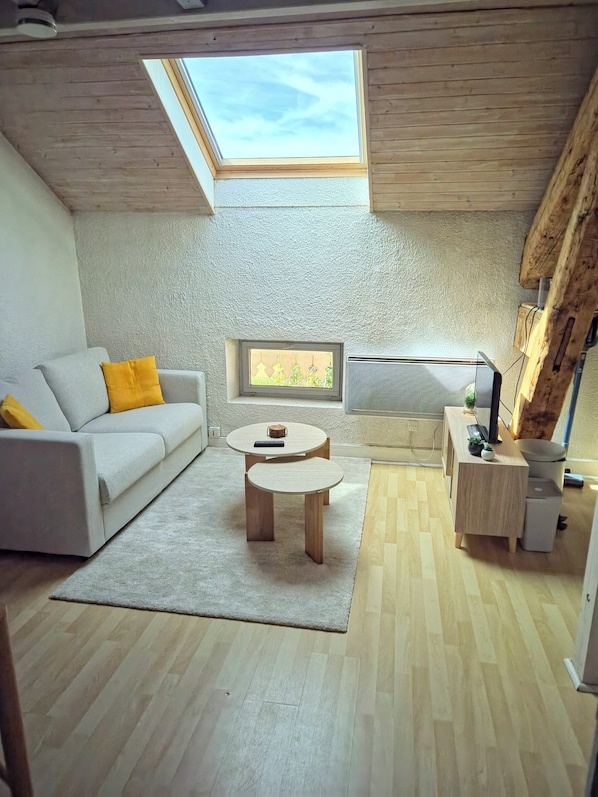 A modern living room with a sloped ceiling, a sofa with yellow cushions, a coffee table, a television, and a small side table with a plant.
