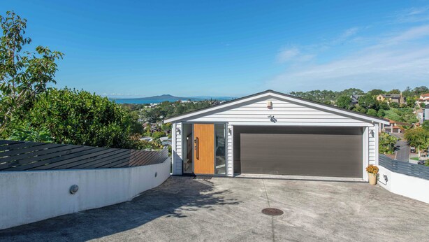 Un garage moderne avec une porte en bois, une allée en béton et une vue dégagée sur un quartier résidentiel et des collines en arrière-plan.
