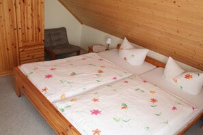 Ein Schlafzimmer mit einem Holzbettgestell, zwei Einzelbetten, einem Sessel und einem kleinen Nachttisch mit Lampe.