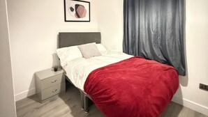A bedroom with a bed, a nightstand, a drawer, a framed picture on the wall, and a window with curtains. - Chatham 5-bed House, Sleeps 10 w/ Parking & Garden (Chatham)