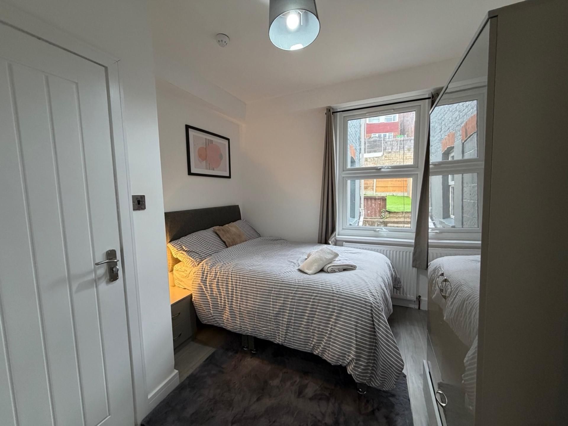Een slaapkamer met een bed, nachtkastje, raam en deur.