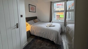 A bedroom with a bed, a bedside table, a window, and a door. - Spacious 5-bedroom Home in Chatham With Private Garden Sleeps 7 (Chatham)