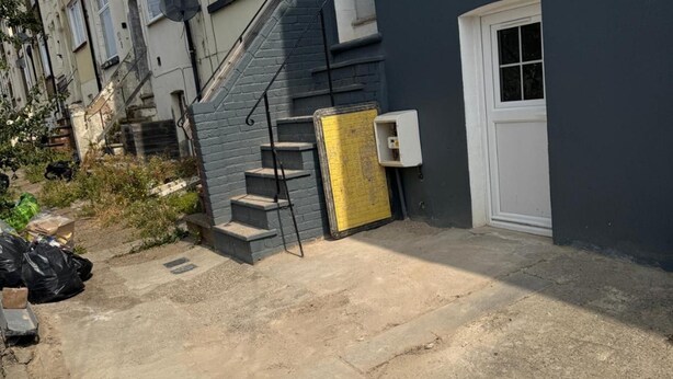 A residential building with a set of concrete steps leading to a door, a satellite dish on the roof, and a small outdoor area with a yellow door. - Spacious 5-bedroom Home in Chatham With Private Garden Sleeps 7 (Chatham)