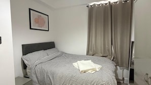 A bedroom with a bed, a nightstand, a framed picture on the wall, and a window with curtains. - Chatham 5-bed House, Sleeps 10 w/ Parking & Garden (Chatham)