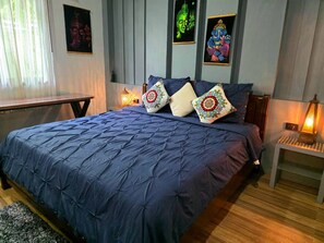 A bedroom with a large bed, a bedside table, a lamp, and wall art.