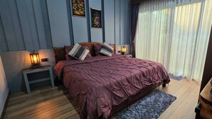 A bedroom with a bed, bedside lamps, a nightstand, a window with curtains, and a wooden floor.