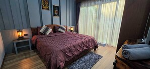 Een slaapkamer met een bed, bedlampen, een nachtkastje, een raam met gordijnen en een houten vloer.