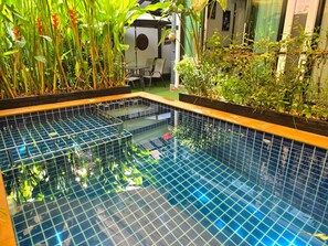 An indoor swimming pool with tiled walls and a wooden border, surrounded by lush greenery and a seating area.