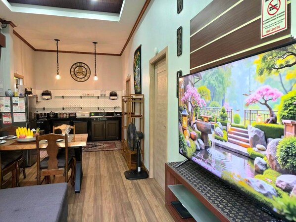 A modern living room with a flat-screen TV, wooden furniture, and a kitchen in the background.