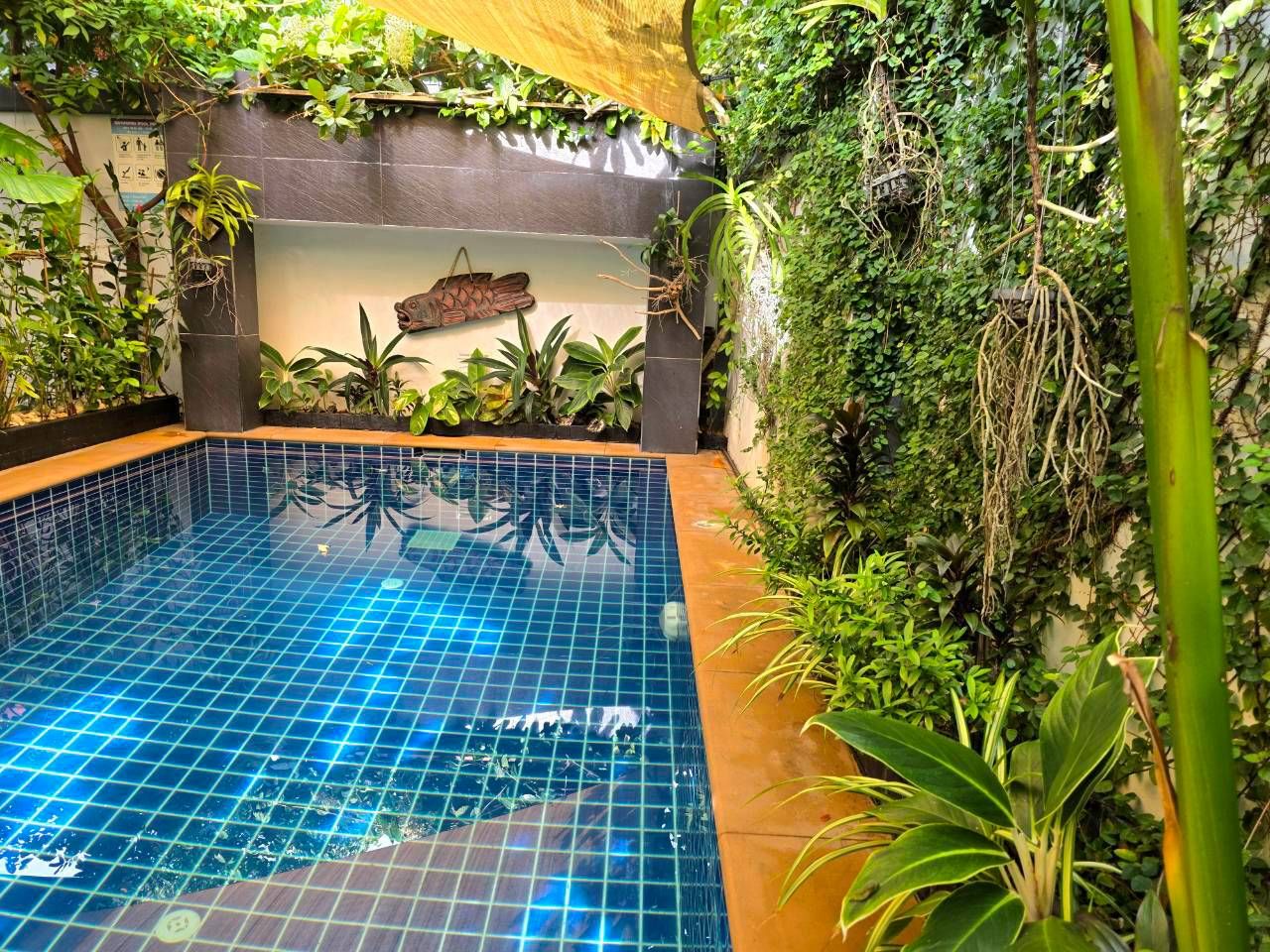 Une piscine intérieure dotée d’un sol carrelé, entourée d’une végétation luxuriante et agrémentée d’un mur décoratif.