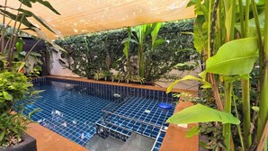 An indoor swimming pool with a tiled floor, surrounded by lush greenery and a wooden deck.