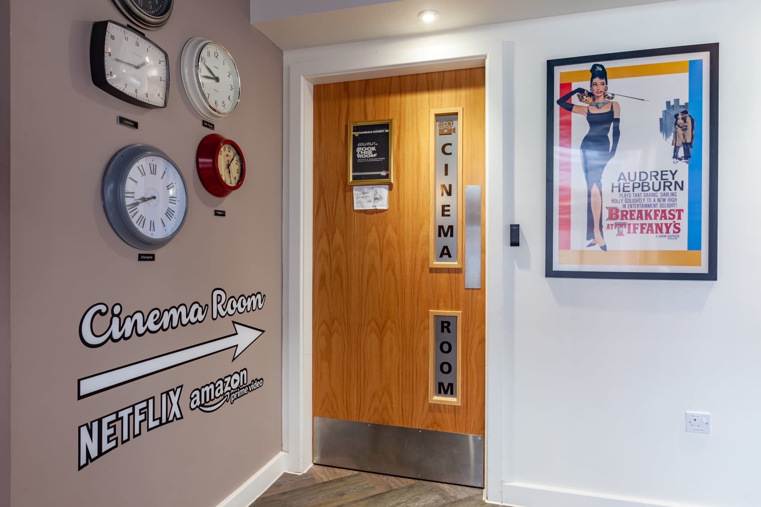 A hallway with clocks on the wall, a cinema room sign, and a poster for a movie.