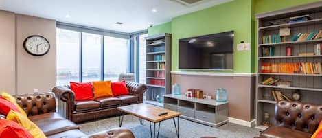 Una sala de estar moderna con sofás de cuero, una mesa de centro, una estantería y un televisor de pantalla plana.