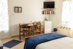 Un dormitorio con cama, escritorio, sillas, televisor y estantería.