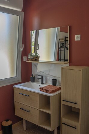 Un baño con un lavabo blanco, un espejo encima, un mueble de madera y una ventana con vidrio esmerilado.
