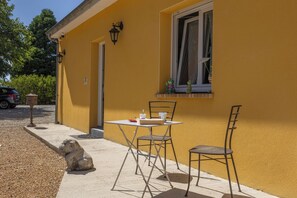 Un edificio amarillo con una ventana, una mesa con sillas y una escultura de piedra en el suelo.