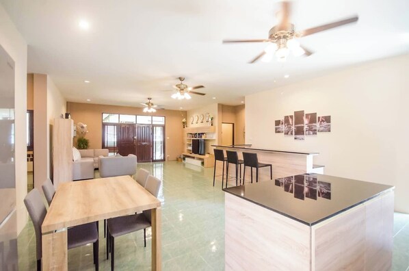 Una cucina moderna con isola centrale, zona pranzo con tavolo e sedie, e zona living con divano e televisore.