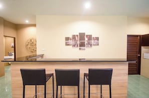 Un área de recepción con mostrador, tres sillas tipo bar y una obra de arte colgada en la pared.
