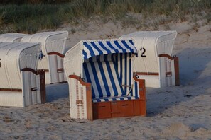 Eine Reihe von Strandstühlen mit einem gestreiftem Sonnendach, mit Nummern versehen und auf einem Sandstrand aufgereiht.