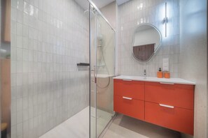 A modern bathroom with white tiled walls, a glass shower enclosure, and a red vanity with a mirror. - Kierbedzia Boutique Studio, Mokotów, Warsaw (Warszawa)