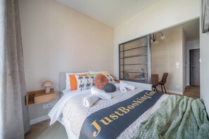 A neatly made bed with a 'JustBooking' blanket, a bedside lamp, and a nightstand. - Kierbedzia Boutique Studio, Mokotów, Warsaw (Warszawa)