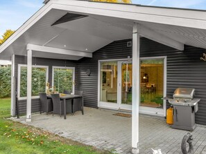 A covered patio area with a table and chairs, a grill, and a sliding glass door leading to an interior space. - "Alkmar" -  from the sea by Interhome (Hals)