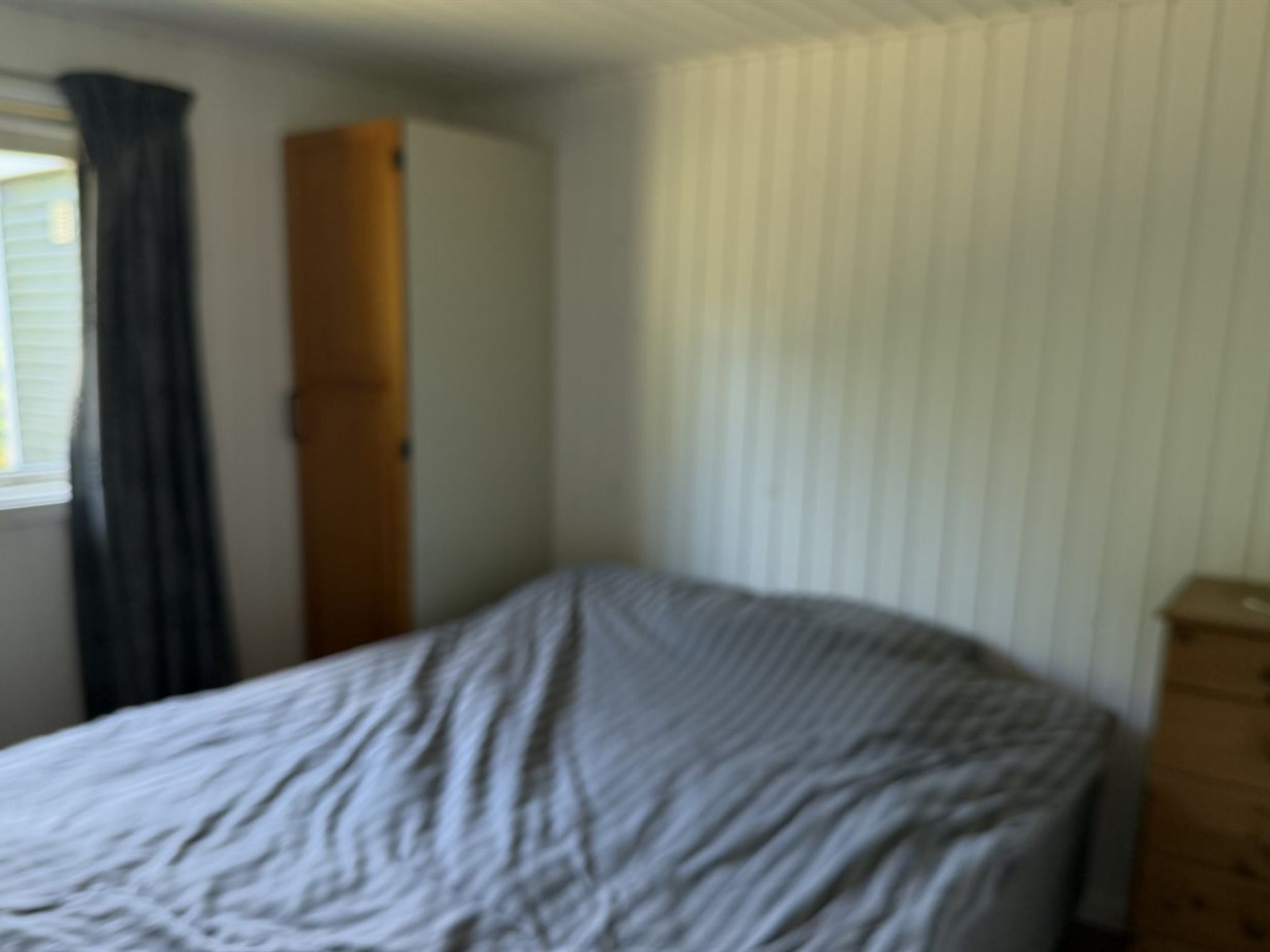 Ein Zimmer mit einem Bett, einem Vorhangfenster und einem Holzkleiderschrank.