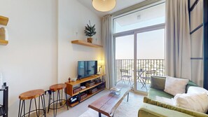 A modern living room with a flat-screen TV, wooden furniture, and a balcony with outdoor seating. - Chic 1 Bed l Walking Distance to Dubai Hills Mall (Dubai)