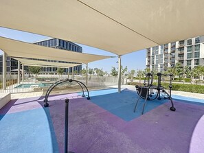 An outdoor exercise area with a pool, exercise equipment, and a covered seating area. - Chic 1 Bed l Walking Distance to Dubai Hills Mall (Dubai)