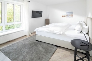 Ein modernes Schlafzimmer mit Bett, Wandfernseher und einem fenster mit Vorhängen.