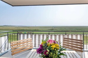 Ein Balkon mit einer Holzbank, Blumenarrangements und Blick auf eine flache Landschaft.