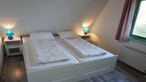 Quarto duplo com duas camas, mesas de cabeceira, abajures e janela com cortinas.