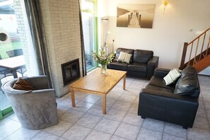 A living room with a sofa, a coffee table, a fireplace, and a staircase. - Holiday home with 3 bedrooms (Julianadorp)