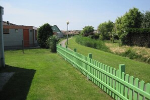Une clôture verte, un chemin et un bâtiment avec une porte rouge.