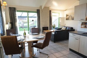 A modern kitchen with a dining area, a fireplace, and a view of the outdoors. - Holiday home with 3 bedrooms (Julianadorp)