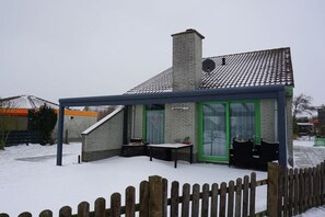 A small building with a brick chimney, a covered outdoor seating area, and a wooden fence. - Holiday home with 3 bedrooms (Julianadorp)