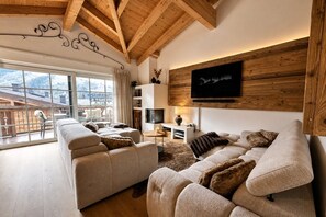 Uma sala de estar moderna com uma janela ampla, vigas de madeira no teto, uma TV de tela plana e um espaço de estar aconchegante.