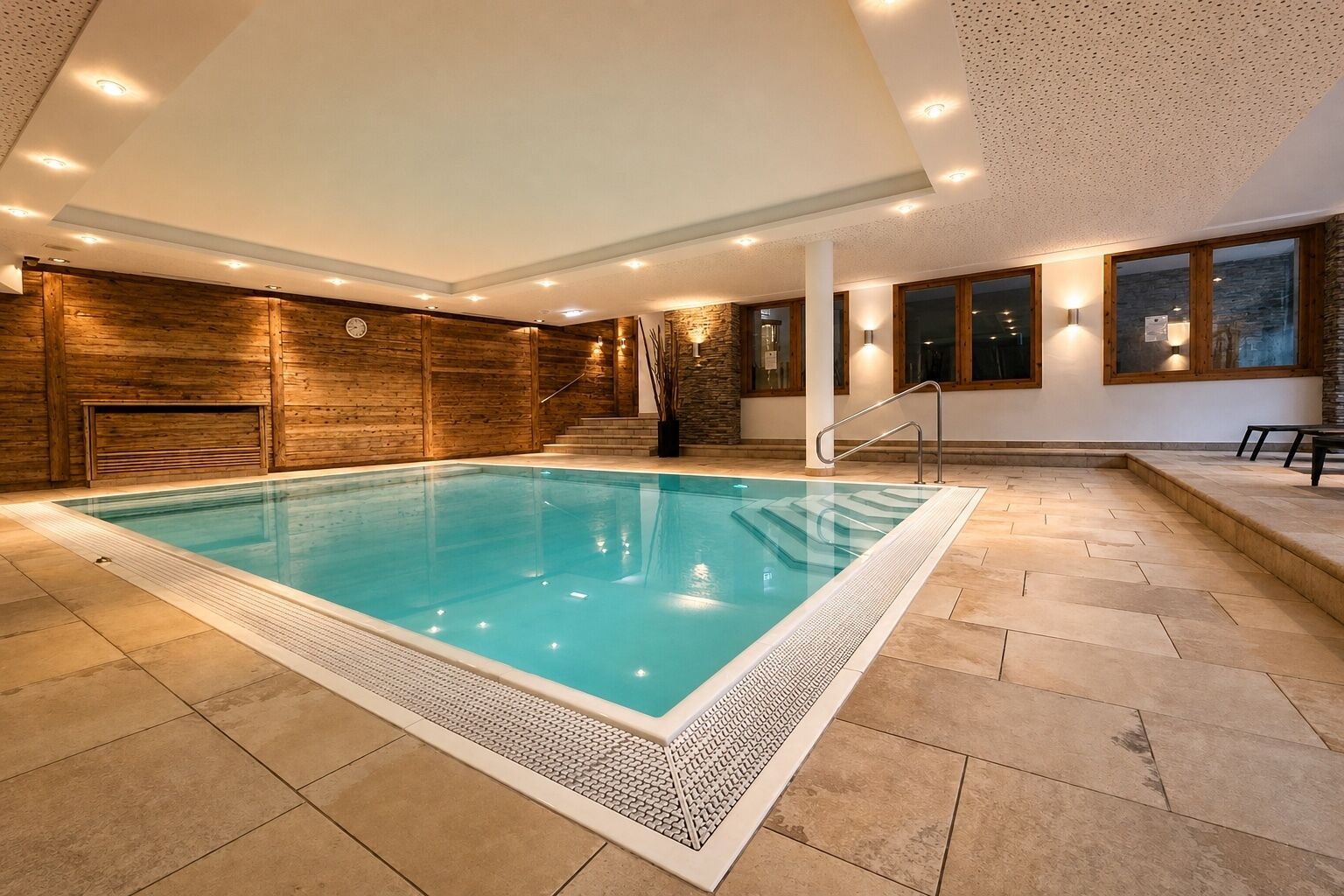 A swimming pool with a wooden wall and a stone wall, surrounded by a tiled floor.