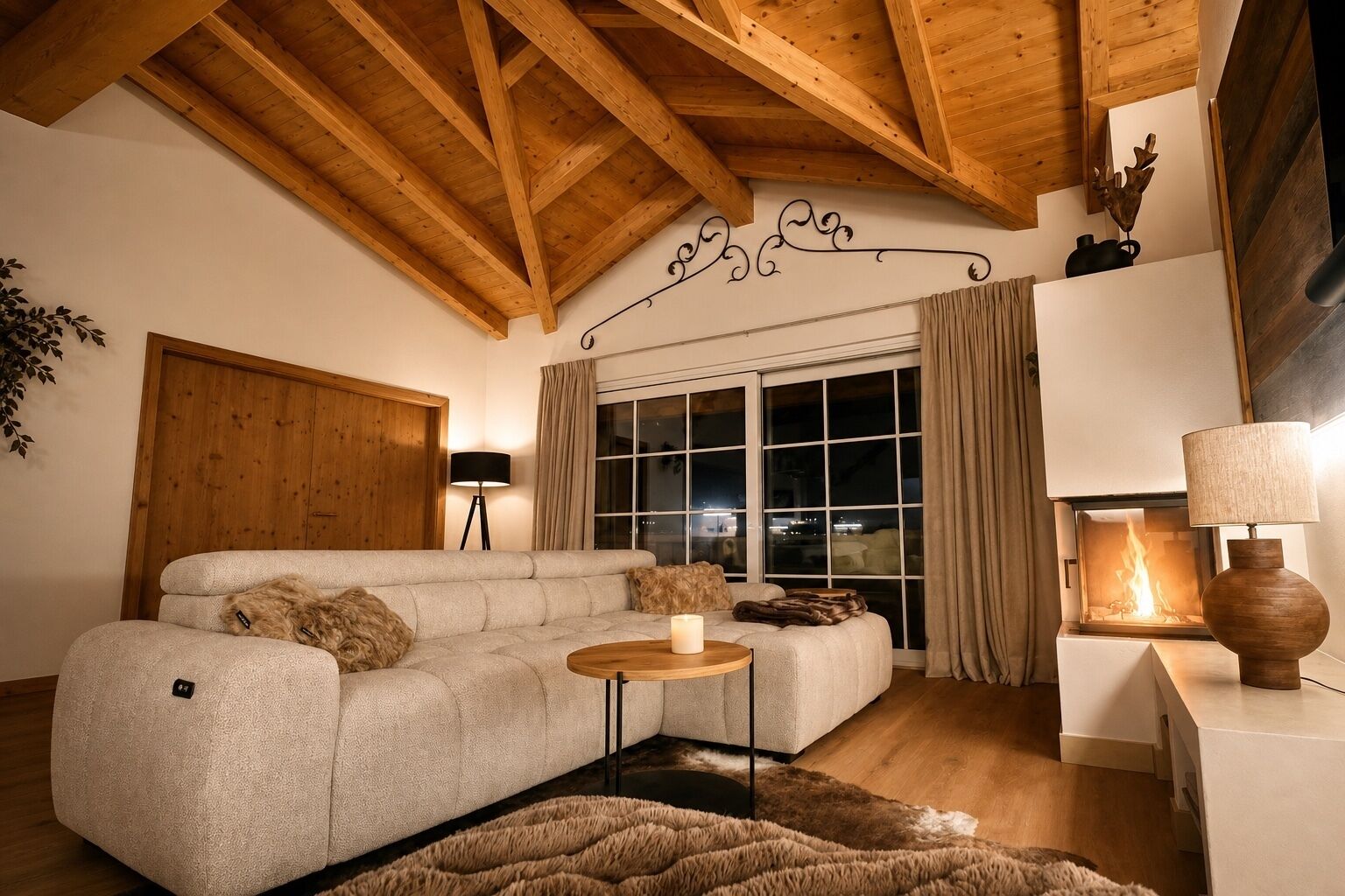 A cozy living room with a sectional sofa, a small round table, a fireplace, and a wooden ceiling.